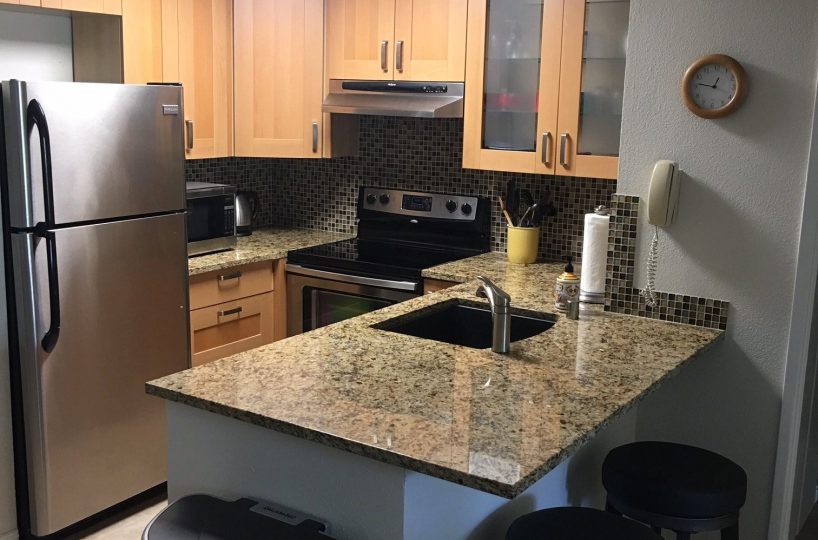 Unit F-106 Kitchen with stainless steel appliances, and breakfast bar with 2 stools