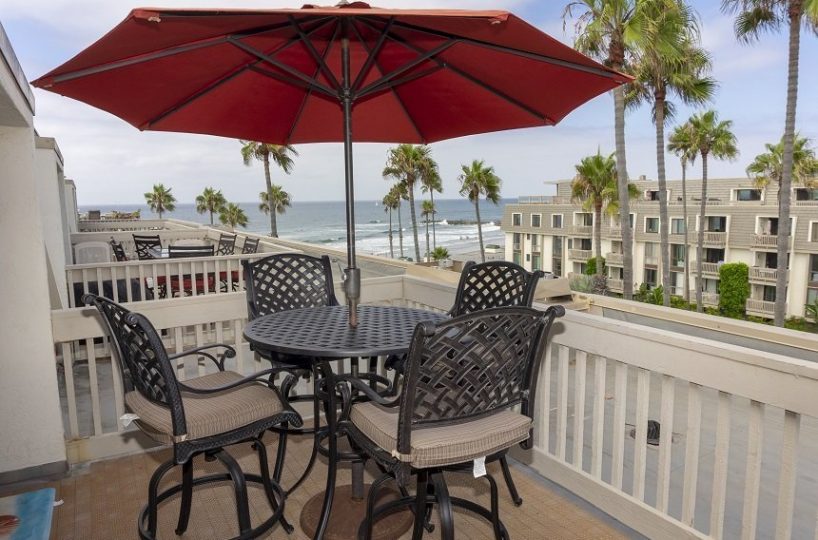 large patio with 4 chairs and a table with red umbrella overlooking the pacific ocean